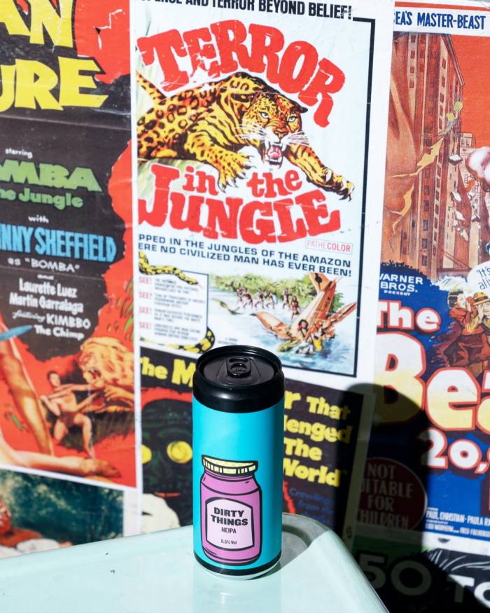 Una lata de cerveza Dirty Things de Jungle Juice Brewing frente a carteles retro de películas B