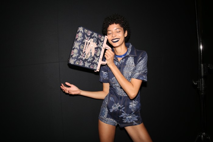 A model wears a tapestry-inspired outfit and holding a matching bag