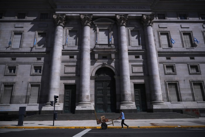 A man pushes a cart past the front door of the National Bank of Argentina in Buenos Aires