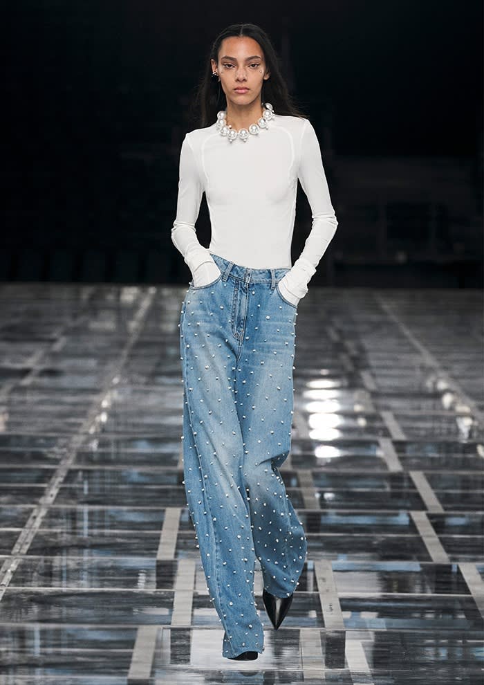 A slim female catwalk model in a tight white top and loose-fitting studded blue jeans