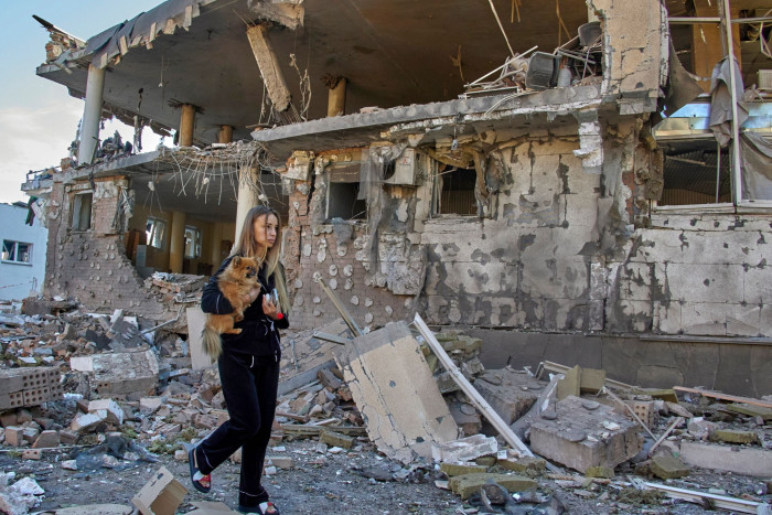 A woman holding a dog next to a damaged building