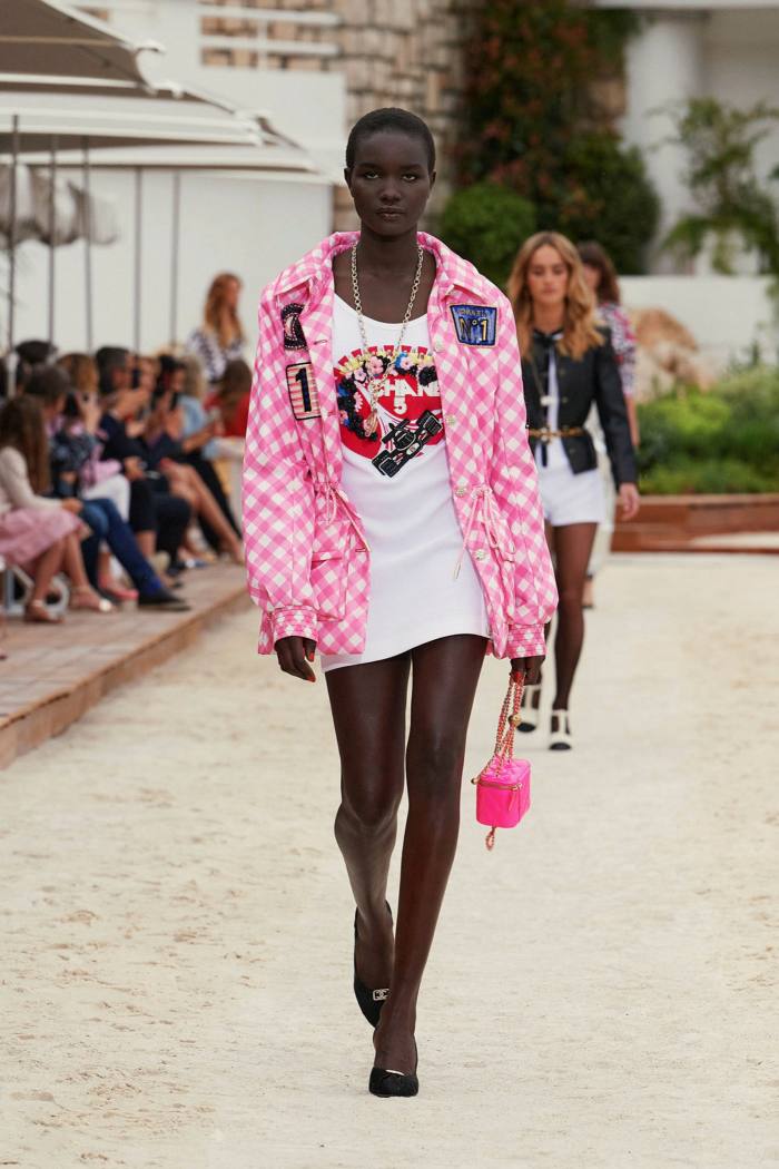 A model in short white dress and pink-and-white checkered jacket