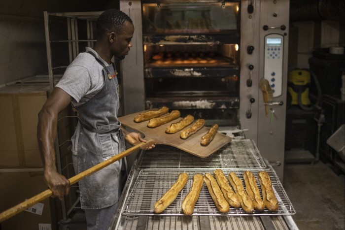 A baker takes baguettes out of an oven in Paris