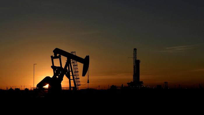A pump jack in front of a drilling rig at sunset in Midland, Texas