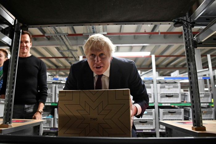 UK Prime Minister Boris Johnson moves a box in a THG fulfillment centre