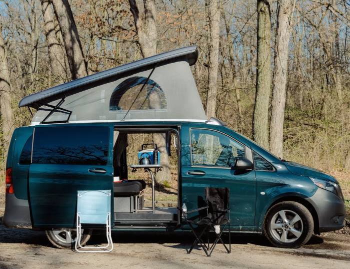 The Mercedes-Benz Metris, parked in front of a backdrop of trees, with its doors open and extendable roof top popped up