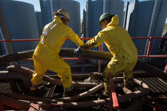 Floor hands wearing yellow protective gear work at connecting tubes on an oil drilling rig