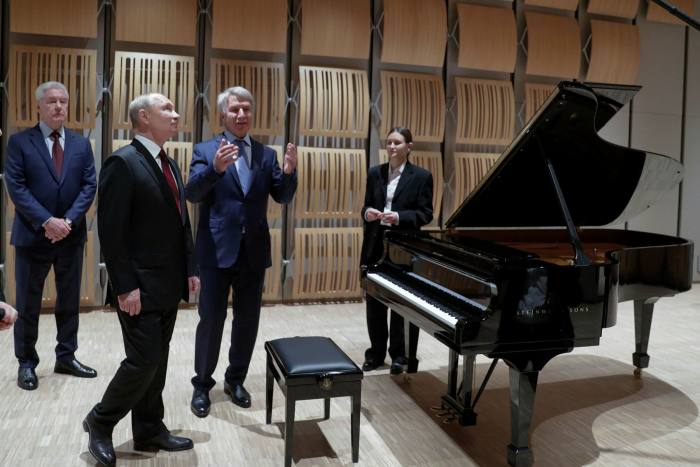 Putin and other men in suits standing close to a grand piano