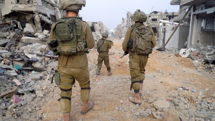 IDF soldiers walk past debris and damaged buildings