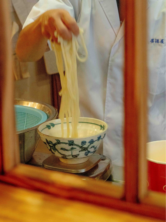 A hand holding udon noodles over a bowl at Frankfurt's Mangetsu restaurant