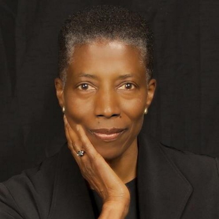 A portrait of a black woman with short, greying hair, her chin resting on one hand