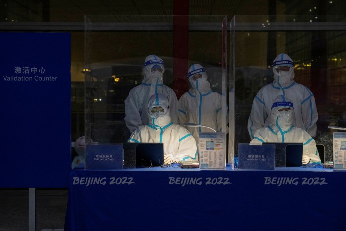 A photo of officials in personal protective equipment waiting to validate Olympic accreditation at Beijing airport