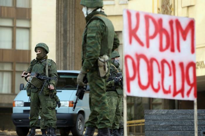Unidentified troops outside the Crimean parliament building in March 2014 next to a sign that reads ‘Crimea Russia’