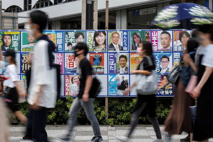 Yayalar, Pazar günü Tokyo'da Japonya'nın üst meclis seçimleri için kampanya afişlerinin yanından geçiyorlar
