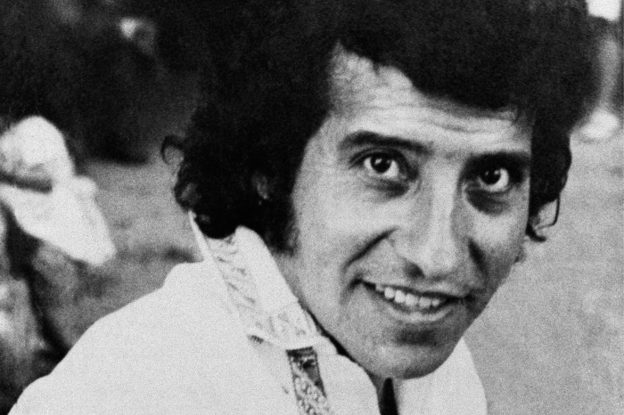 صورة بالأبيض والأسود من أوائل السبعينيات لناشط ومغني وكاتب أغاني تشيلي طويل الشعر فيكتور جارا يرتدي قميصًا أبيض