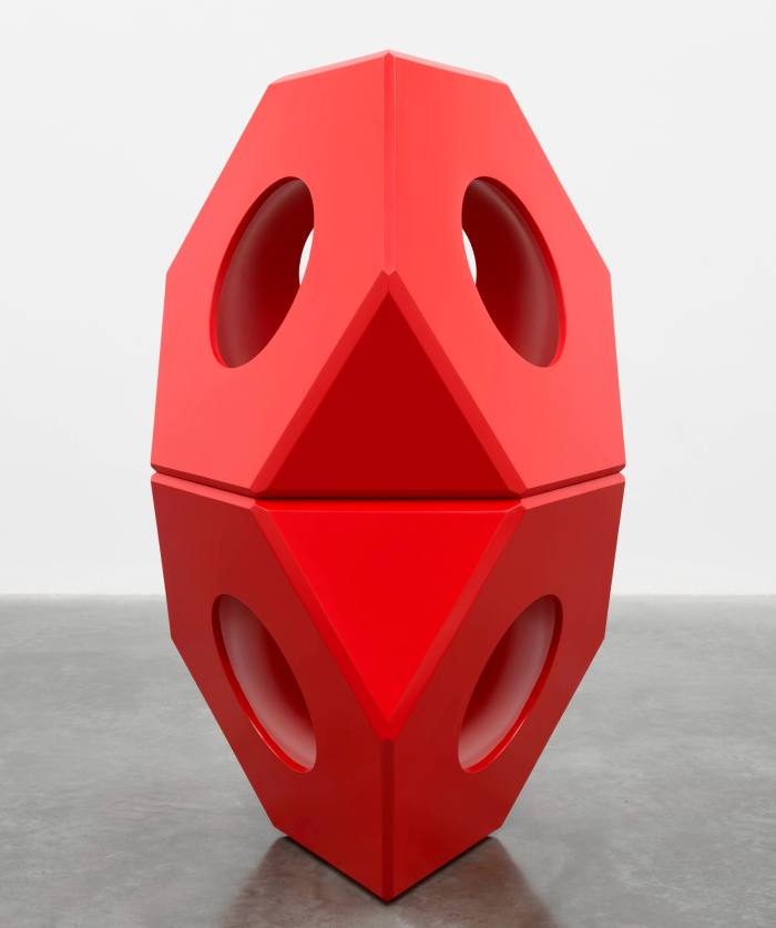 Una gran escultura roja formada por dos formas geométricas apiladas atravesadas por agujeros. 