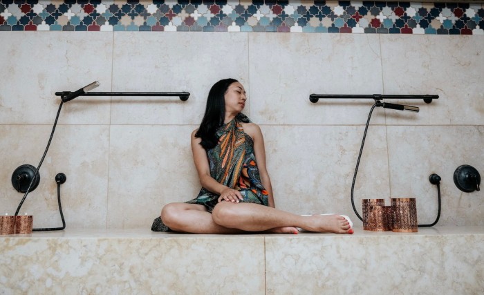 Một người phụ nữ ngồi xuống, dựa lưng vào bức tường lát gạch, trong phòng tắm hammam của spa