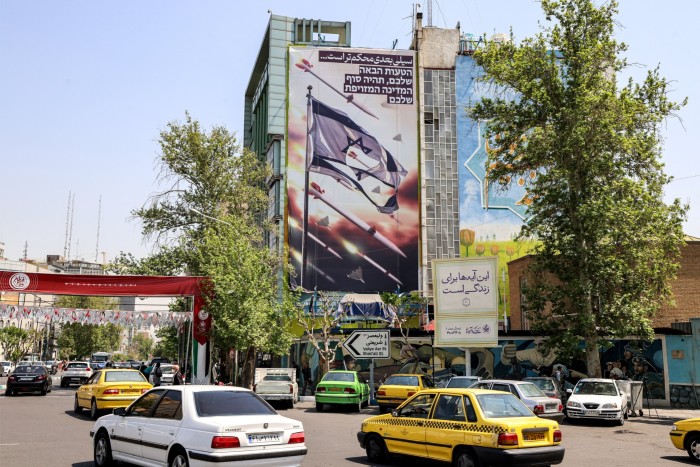 Cars move past a building with a banner depicting missiles and drones flying past a torn Israeli flag on April 14