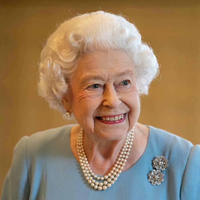 The Queen in 2022. She is smiling, wearing a light blue dress and pearls. Her hair is white