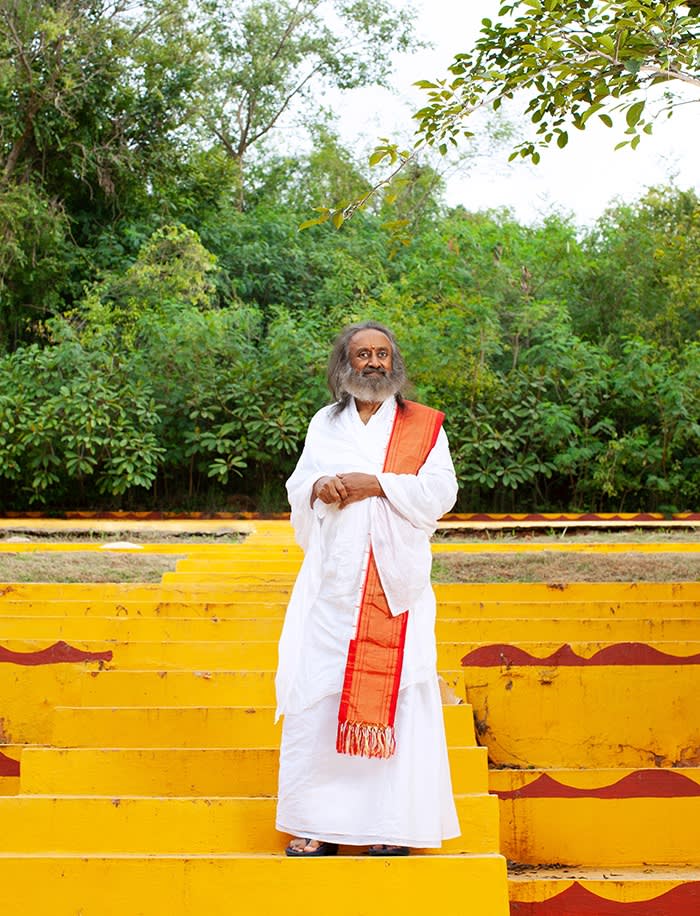 Gurudev Sri Sri Ravi Shankar on. the yellow steps at his ashram in Bangalore, India, in August. As well as his white robes he has a bright orange sash draped over one shoulder and is smiling at the camera 