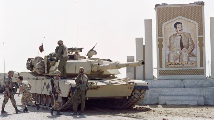 Soldier stands around an Abrams M1/A1 tank below a picture of Iraqi President Saddam Hussein on the outskirts of Kuwait city on March 1 1991