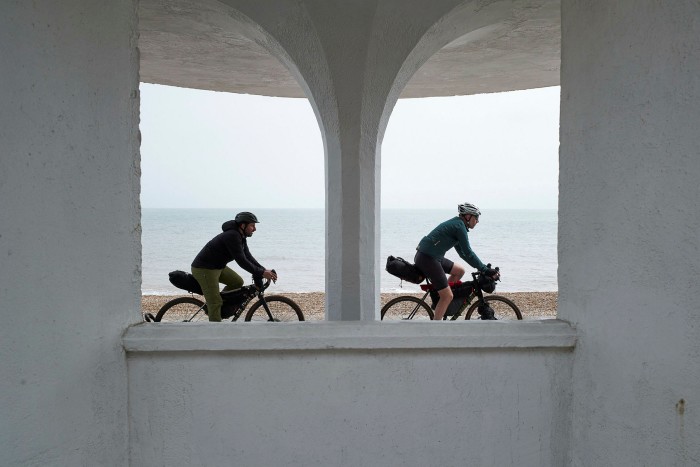 Cyclists, seen through the arches of a shelter by the beach