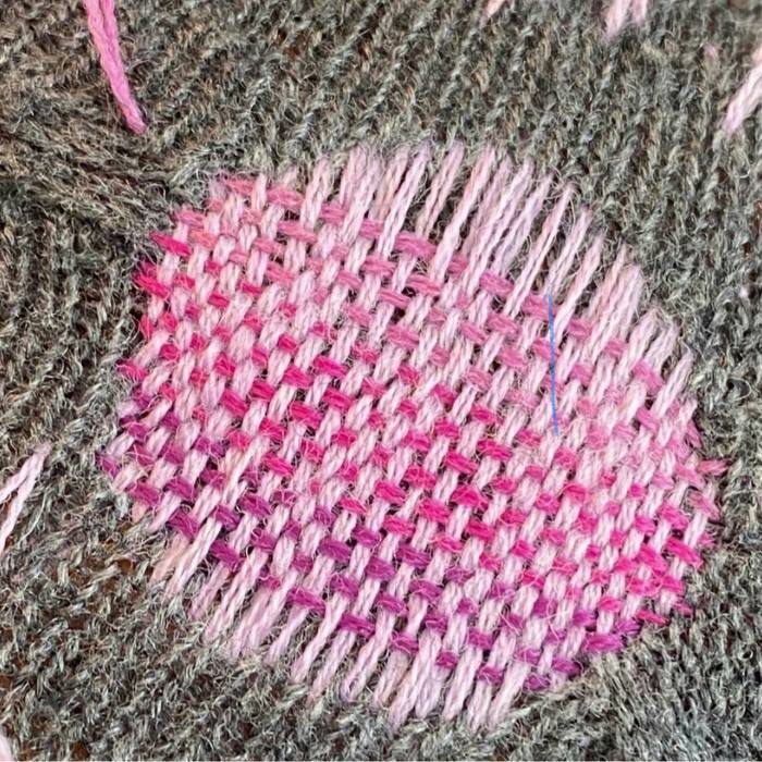 A close-up of a hole in a piece of clothing repaired by Zetuni with pink and purple needlework