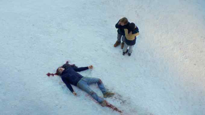 Seen from above, a man lies in the snow with blood surrounding his head while two people lookon