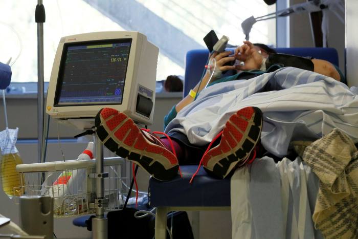 A woman wearing an oxygen mask sits on a bed in a makeshift emergency room in a Bucharest hospital
