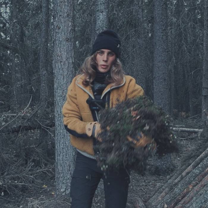 Een vrouw staat in het bos met een arm vol mos en twijgen