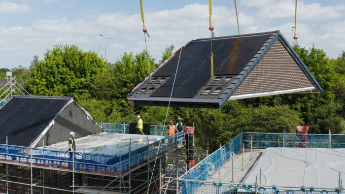 A crane lifts a solar panelled roof unit to the top of a building
