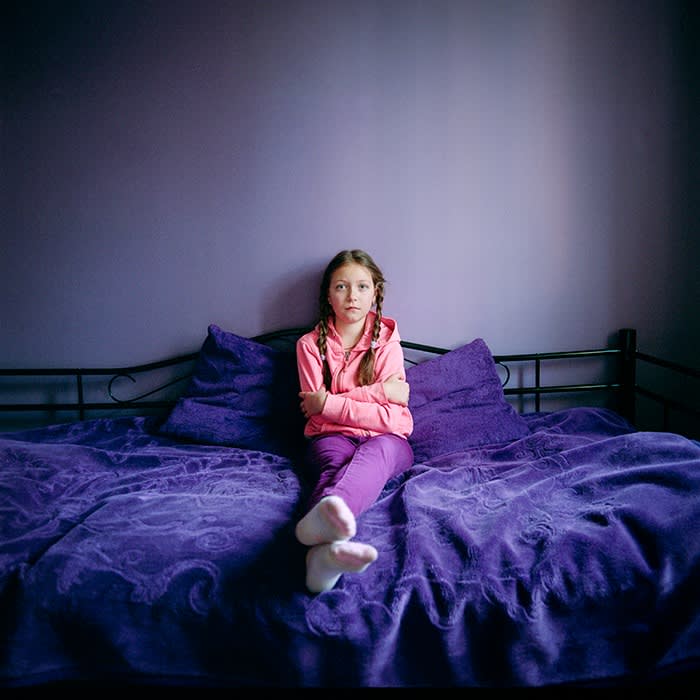 Margarita Mykhailenko sitting on a bed with purple sheets