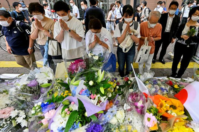 İnsanlar Shinzo Abe'nin vurularak öldürüldüğü yerin yakınındaki derme çatma bir anma töreninde dua ediyor