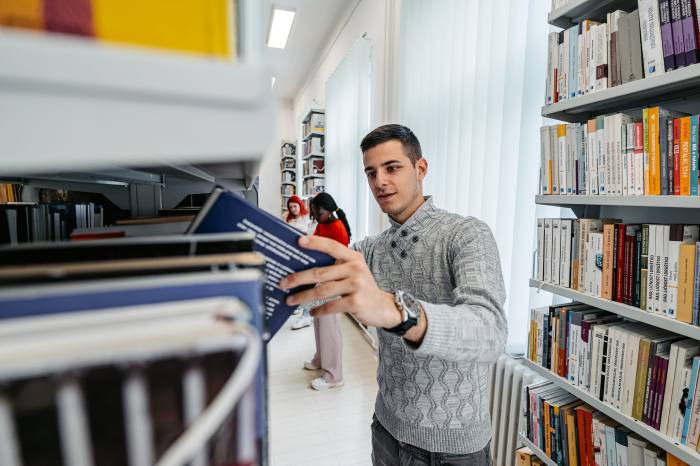 Male student picking out a book in a college library