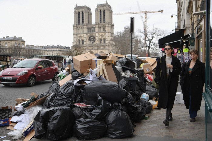 Pedestrians walk past full trash cans near Notre Dame Cathedral in Paris 