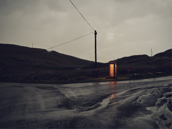 A roadside phone box is illuminated against a darkening sky