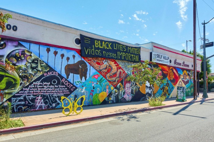 View along a one-storey building frontage brightly painted with animals and plants. Banners hang from the top, one says Black Lives Matter