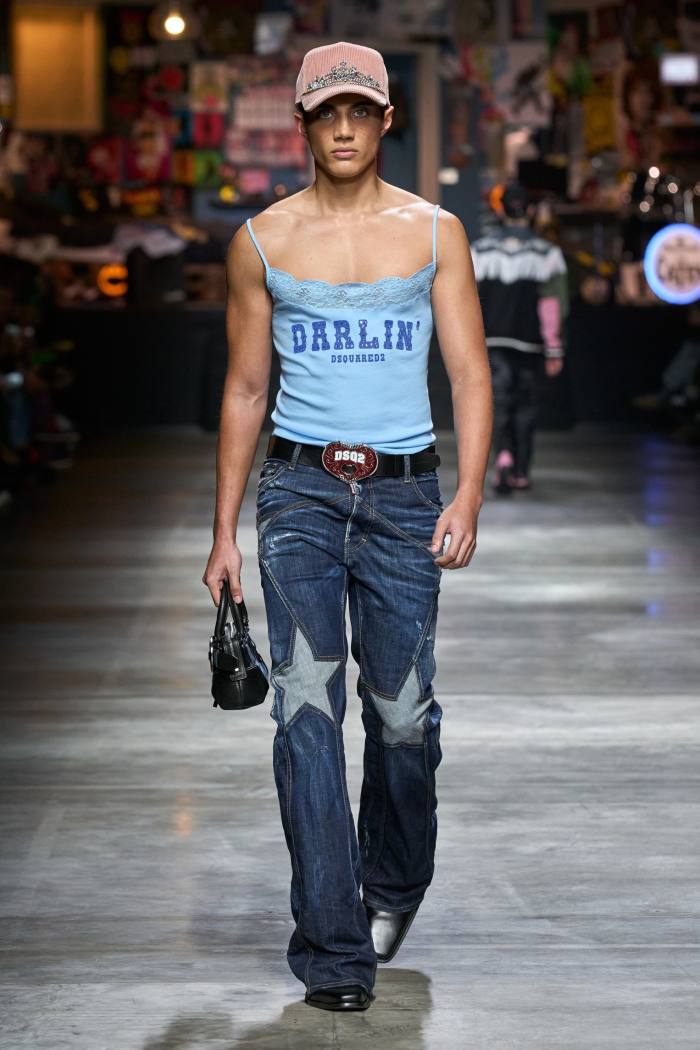 The model wears a cap, low-cut blue vest and jeans with star patterns on the knee