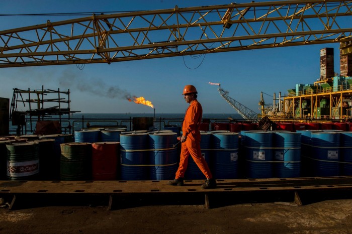 A worker walks past oil drums and gas flares aboard an offshore oil platform operated by National Iranian Offshore Oil Company