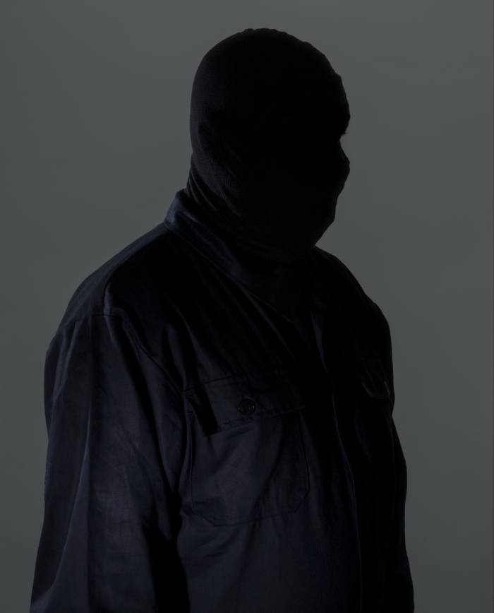 A man dressed in grey and wearing a balaclava standing under overcast skies
