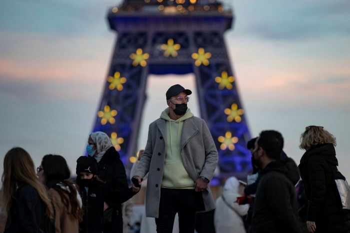 Pedestrians with face masks walk near the Eiffel Tower