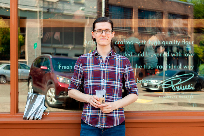 Elizabeth Durand wearing a plaid shirt and glasses stands outside the Roastery
