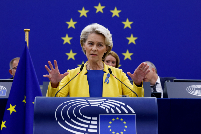 Ursula von der Leyen standing at a lectern, the EU star behind her