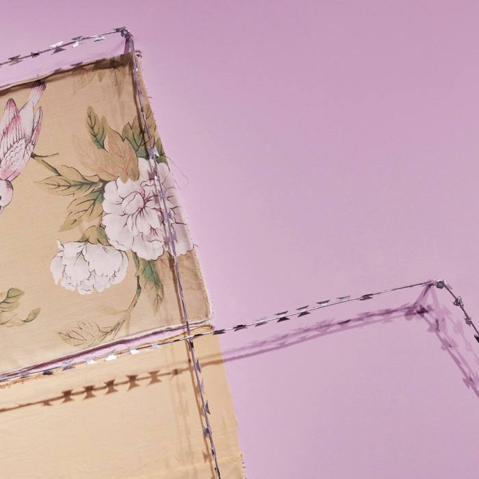 A close-up detail shows the razor wire barbs juxtaposed against floral fabric