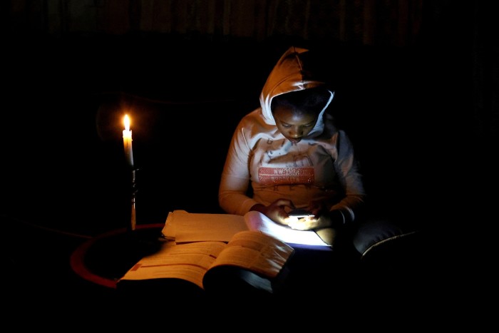 Thandiwe Sithole looks at her mobile phone as she studies by a candle light 