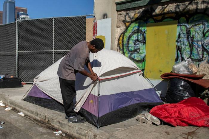 A homeless man zips up his tent in front of the non-profit Midnight Mission’s headquarters
