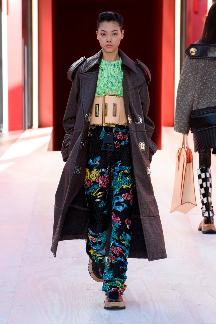 A female catwalk model in a long coat and vibrantly coloured trousers