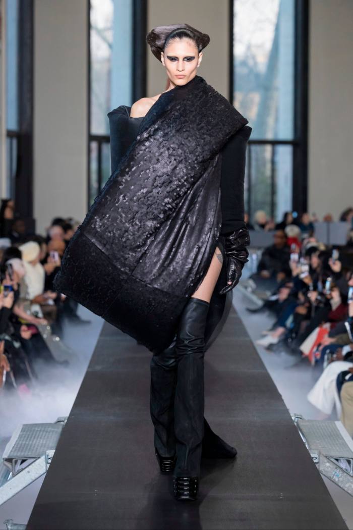 Model in black gown with a large, exaggerated wrap