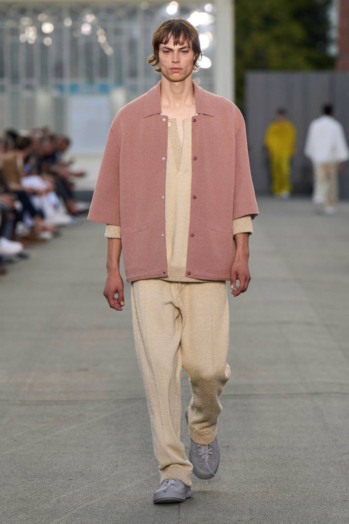 A man models wide beige trousers and pink jacket