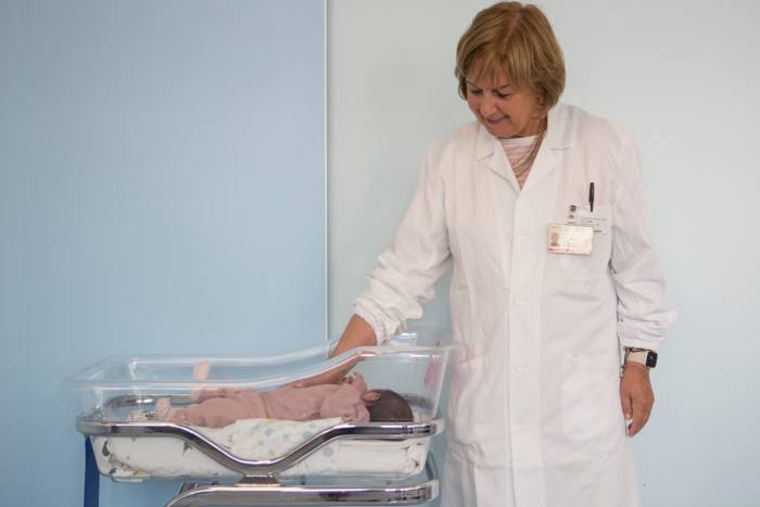 A doctor rests her hand on a newborn’s back in a hospital crib